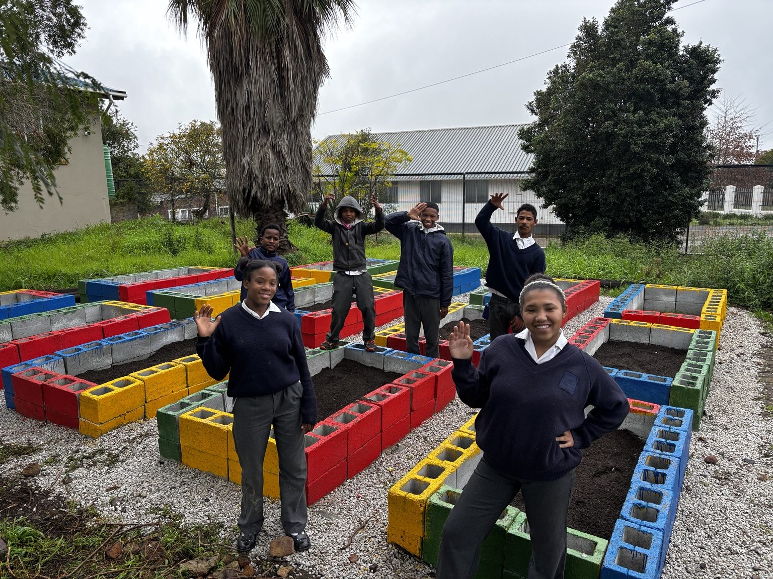 DCAPS learners waving in front of the colourful raised garden beds they built at the school
